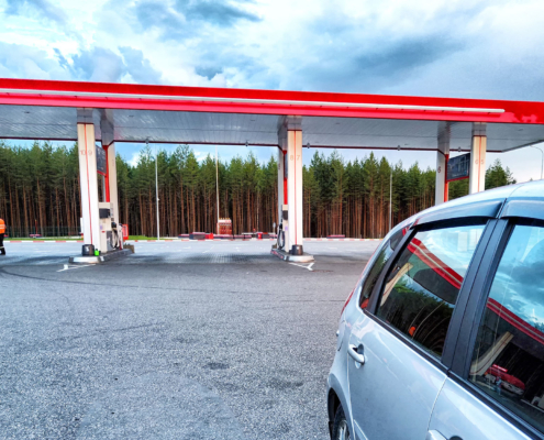 A silver car is parked at a gas station under a cloudy sky